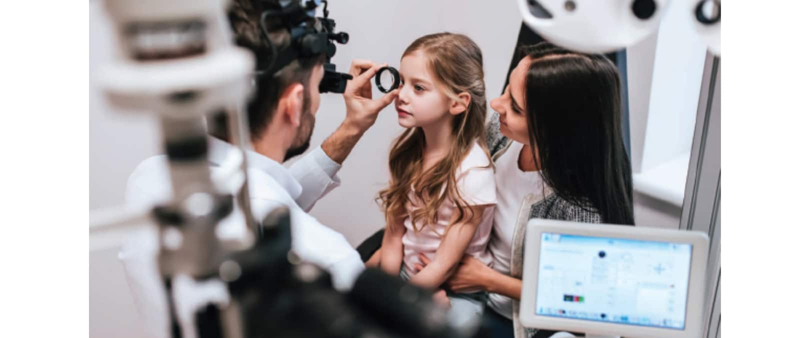 Photograph of a child receiving an eye exam, with her parent close by. Eye exams are one of the first steps to diagnosing and managing childhood myopia.